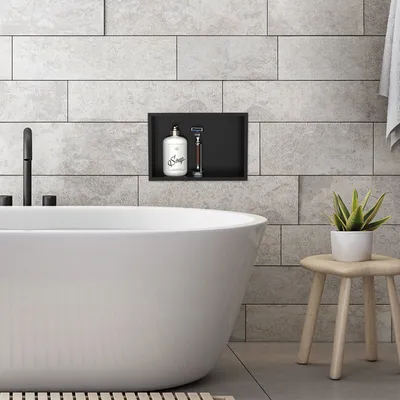 A modern bathroom with a freestanding bathtub, a built-in niche with toiletries, and a small stool with a plant.
