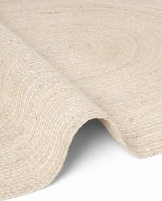 A close-up, angled view of a round jute rug with a braided texture and a spiral pattern.