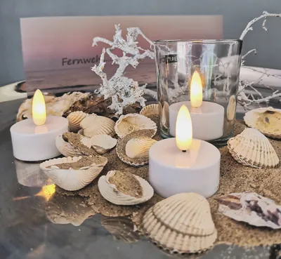 A decorative arrangement of LED tealights, seashells, sand, and driftwood, with a postcard in the background.