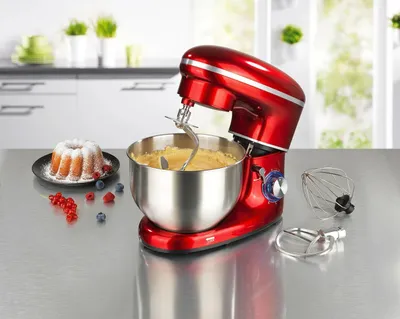 A red stand mixer with a bowl of batter and a bundt cake on a kitchen counter.
