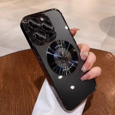 A hand holding a black iPhone case with a metallic ring on a wooden table.