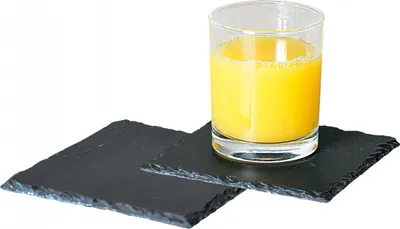 A glass of orange juice sits on two slate coasters.