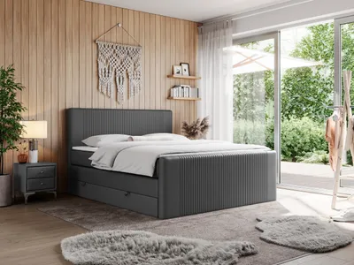A bedroom scene with a dark gray boxspring bed as the main focus, featuring a large sliding glass door leading to an outdoor garden.