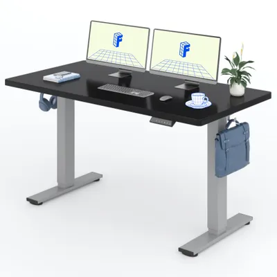 A black height-adjustable desk with dual monitors, keyboard, mouse, headphones, a cup of coffee, and a briefcase hanging from the side.