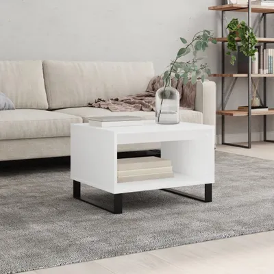 A white coffee table with books and a vase of greenery sits on a grey rug in a living room setting with a beige sofa in the background.