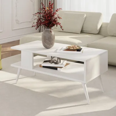 A white coffee table with a vase of red flowers and books on it, placed in a living room setting with a sofa in the background.