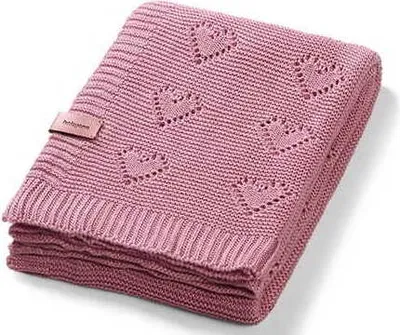 A folded pink knitted baby blanket with a heart pattern and a small tag.