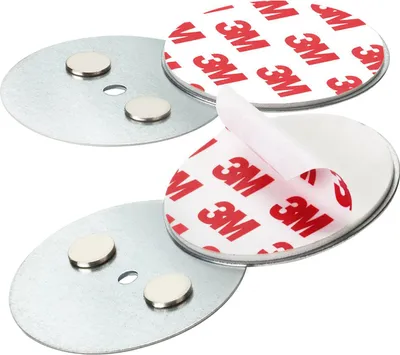 Two round metal plates with magnets and adhesive backing, with the adhesive backing partially peeled off.