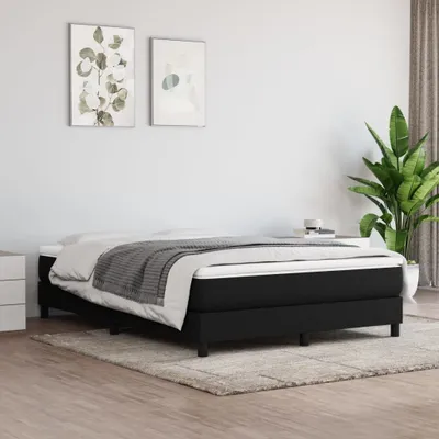A black box spring bed with white and gray bedding, placed on a rug in a room with minimalist wall art and a large plant.