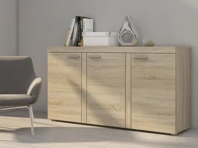 A light brown wooden sideboard with four doors is shown in a room with a grey chair next to it.
