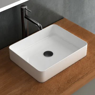 A white rectangular basin sink with a black drain sits on a wooden countertop, with a dark faucet behind it.
