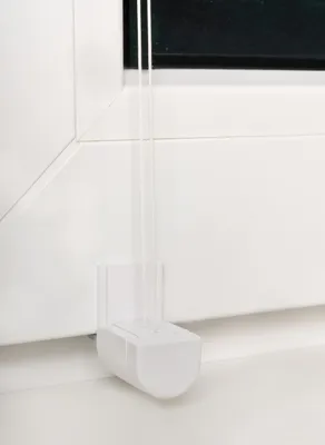 A close-up view of a white window blind cord holder attached to a white window frame.