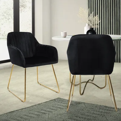 Two black velvet dining chairs with gold legs are shown in a dining room setting.