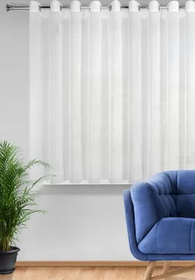 A white sheer curtain hangs on a rod above a windowsill. A blue armchair and a potted plant are in the foreground.