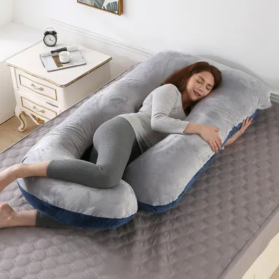 A woman is sleeping on a large U-shaped pregnancy pillow in a bedroom.