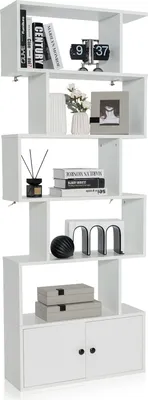 A white, S-shaped bookshelf with five shelves, decorated with books, a clock, a vase with flowers, a picture frame, decorative objects, and storage boxes.