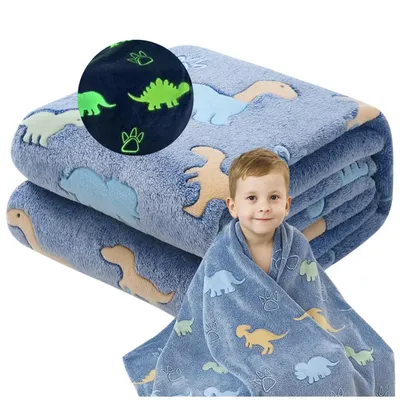 A young boy is wrapped in a blue blanket with dinosaur patterns. The blanket is folded in the background.