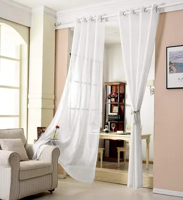 A living room scene with sheer white curtains, a chair, and a dining area in the background.