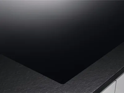 A close-up view of a black glass ceramic hob with a textured gray edge.