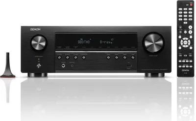 A black Denon AV receiver and its remote control are displayed on a reflective white surface.