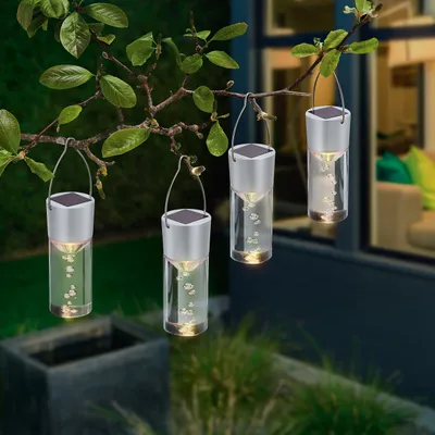 Four solar-powered hanging lanterns with bubbles inside are suspended from a tree branch in a garden setting at dusk.