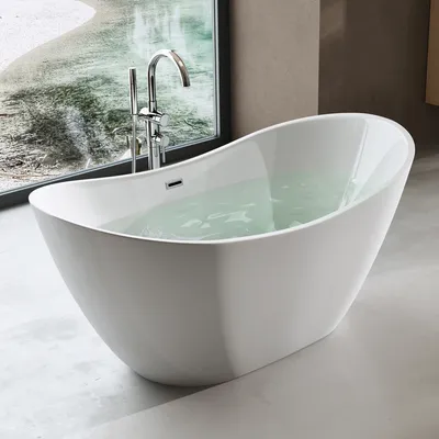 A modern white freestanding bathtub filled with water, placed on a light gray floor next to a large window with a blurred natural scene outside.