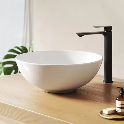 A white ceramic vessel sink with a black faucet on a wooden countertop.