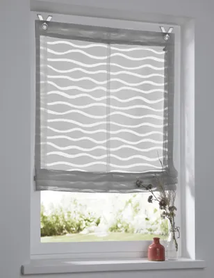A close-up view of a grey Roman blind with a white wave pattern, hanging in a window.