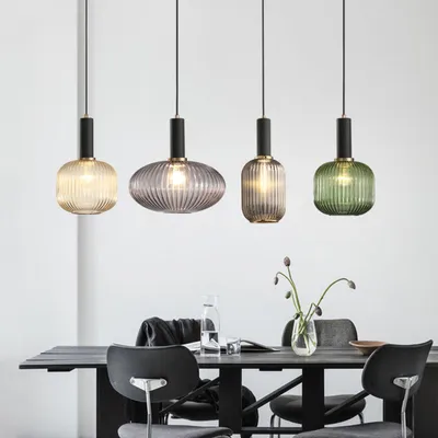 Four glass pendant lights of different colors and shapes hang above a dining table.