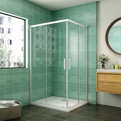 A modern bathroom with a glass shower enclosure, green tiled walls, and a wooden vanity.