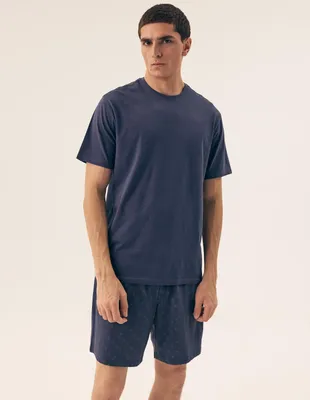 A man is standing and posing for a product photo, wearing a blue t-shirt and blue patterned shorts.