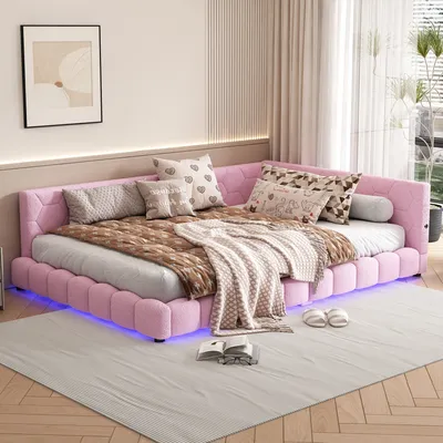 A pink upholstered bed with multiple pillows and blankets, decorated with ambient LED lighting underneath, placed on a wooden floor and a light gray rug.