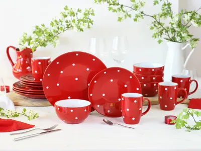 A red and white polka dot dinnerware set arranged on a table with a white pitcher and greenery.