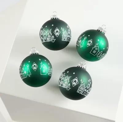 Four green Christmas ornaments with white festive designs are arranged on a white surface.