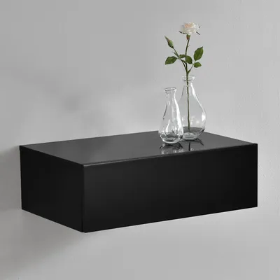 A black floating shelf with two glass vases and a flower on top, mounted on a light gray wall.
