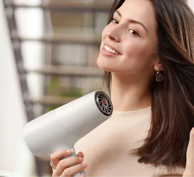 A woman is holding a white hairdryer and styling her hair.