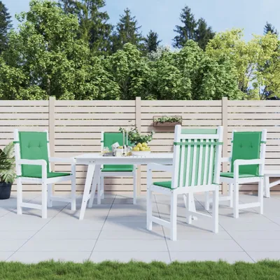 An outdoor patio setting with a white dining table and chairs, adorned with green cushions, set against a backdrop of lush trees and a wooden fence.