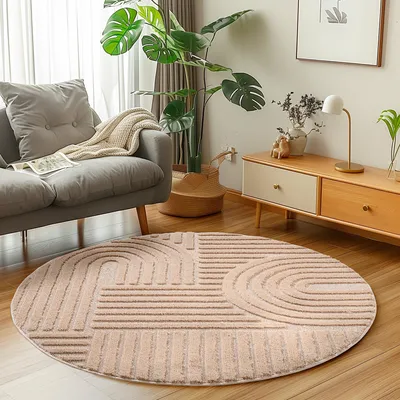 A round rug with a geometric pattern is placed on a wooden floor in a living room setting, next to a gray sofa and a wooden cabinet.