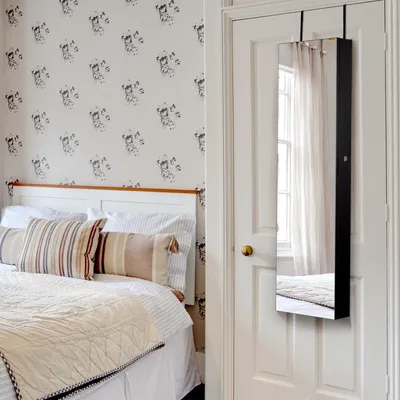 A bedroom scene with a bed and a door with a jewelry cabinet hanging on it.