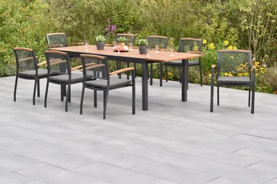 An outdoor dining set with a table and chairs on a patio, surrounded by greenery and flowers.