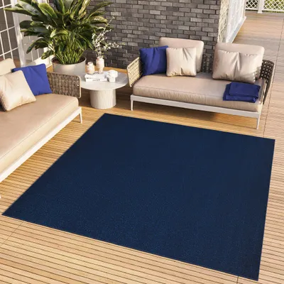 An outdoor patio scene with a navy blue rug, beige sofas, and a coffee table.
