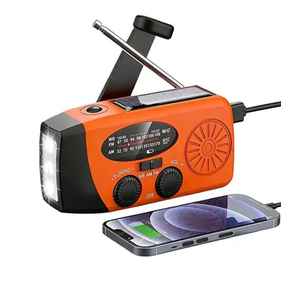 An orange emergency radio with a solar panel and LED flashlight is shown, with a smartphone connected to it for charging.