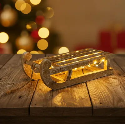 A wooden sled with LED lights on a wooden table, with a blurred Christmas tree in the background.