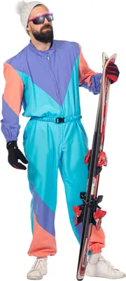 A man wearing a colorful 1980s-style ski suit and holding skis.