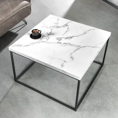 A modern coffee table with a marble-effect top and black metal legs, placed on a concrete floor next to a sofa. A cup of coffee sits on the table.