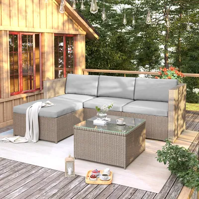 An outdoor patio set with a sectional sofa and coffee table on a wooden deck next to a wooden cabin.
