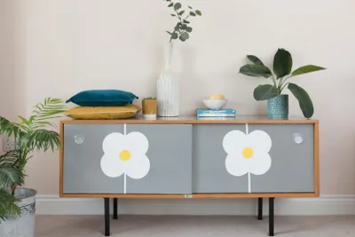 A mid-century modern style sideboard with a floral decal is decorated with cushions, plants, and books.