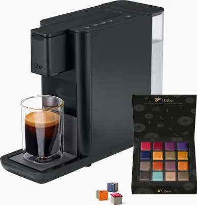 A black Qbo coffee machine with a glass of espresso and a box of coffee capsules.