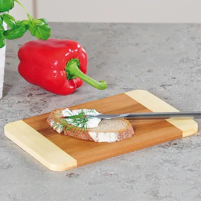 A red bell pepper and a slice of bread with cream cheese and dill on a wooden cutting board.