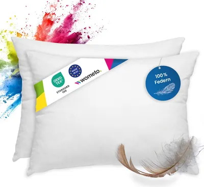 Two white pillows are shown on a white background with colorful powder exploding behind them. There are also tags and a feather on the pillows.